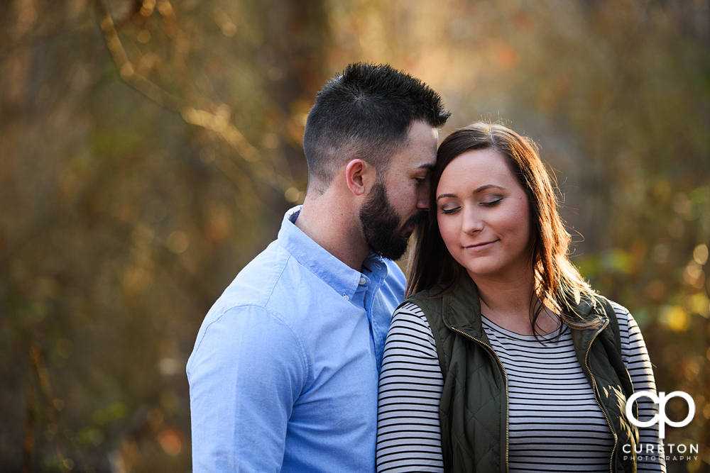 Engaged couple standing in glowing sunlight on the trail.