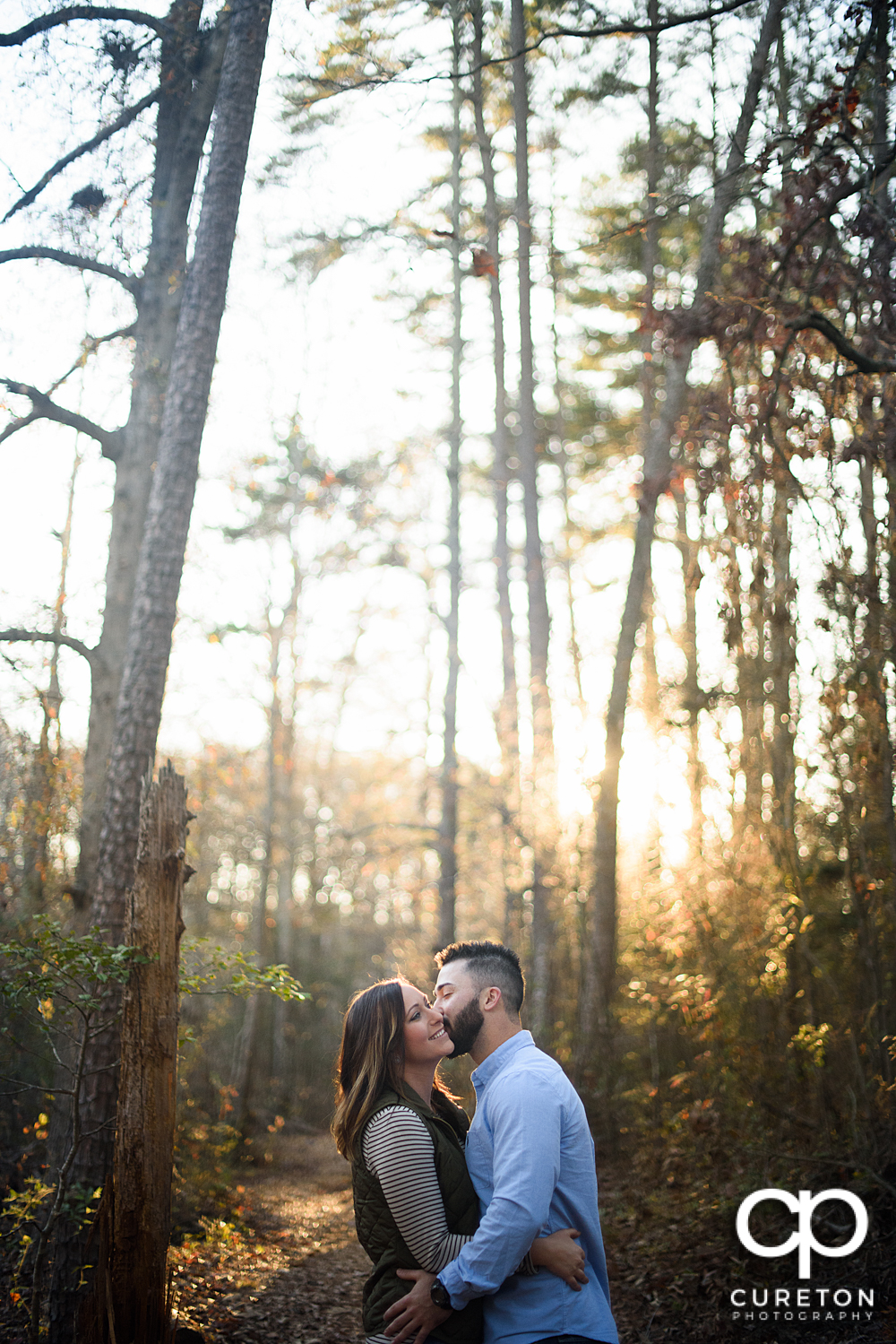 Man kissing his faincee on the cheek during their Lake Conestee Nature Park engagement session..
