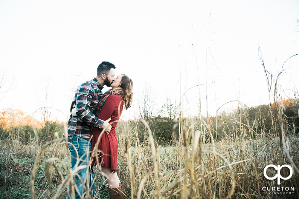Bride and groom kissing in a n open filed during a rustic engagement session in Greenville,SC.