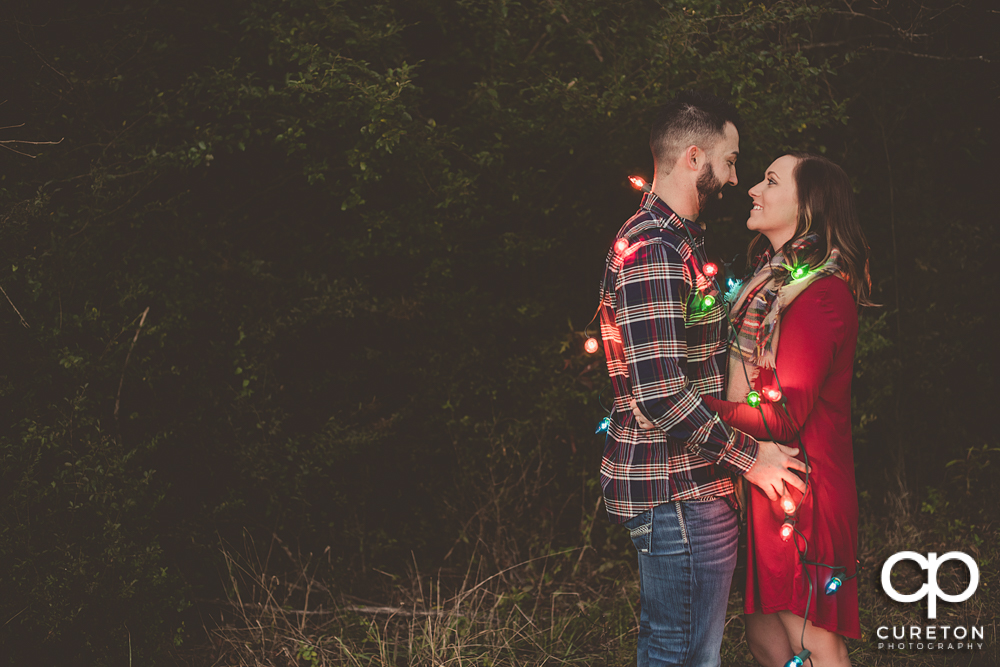 Engaged couple covered in Christmas lights.