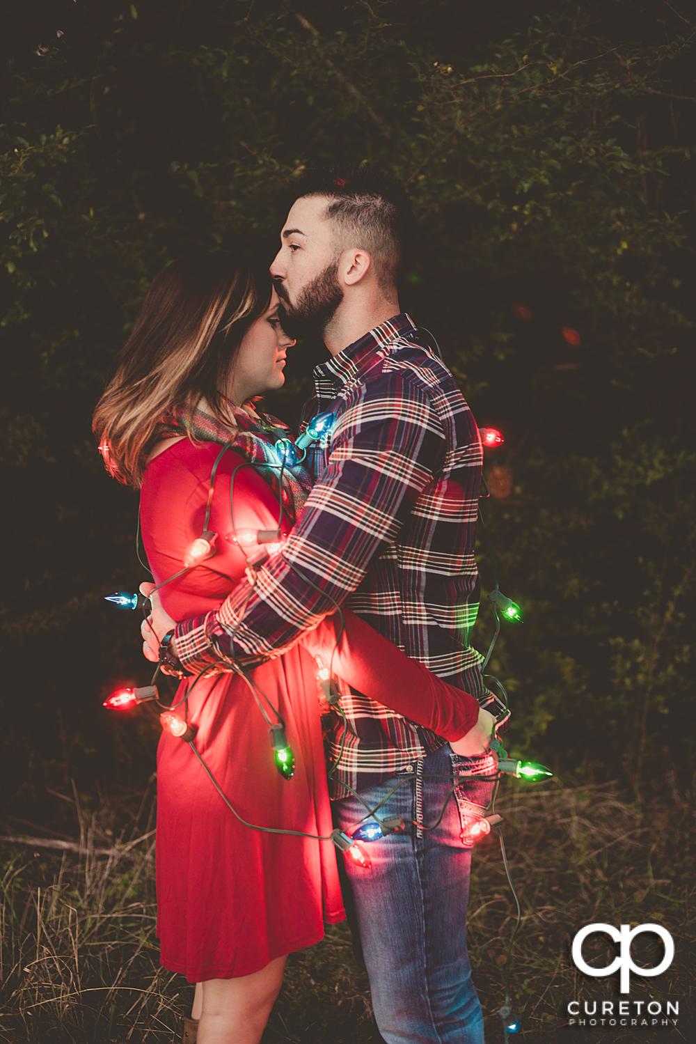 Engaged couple covered in Christmas lights.