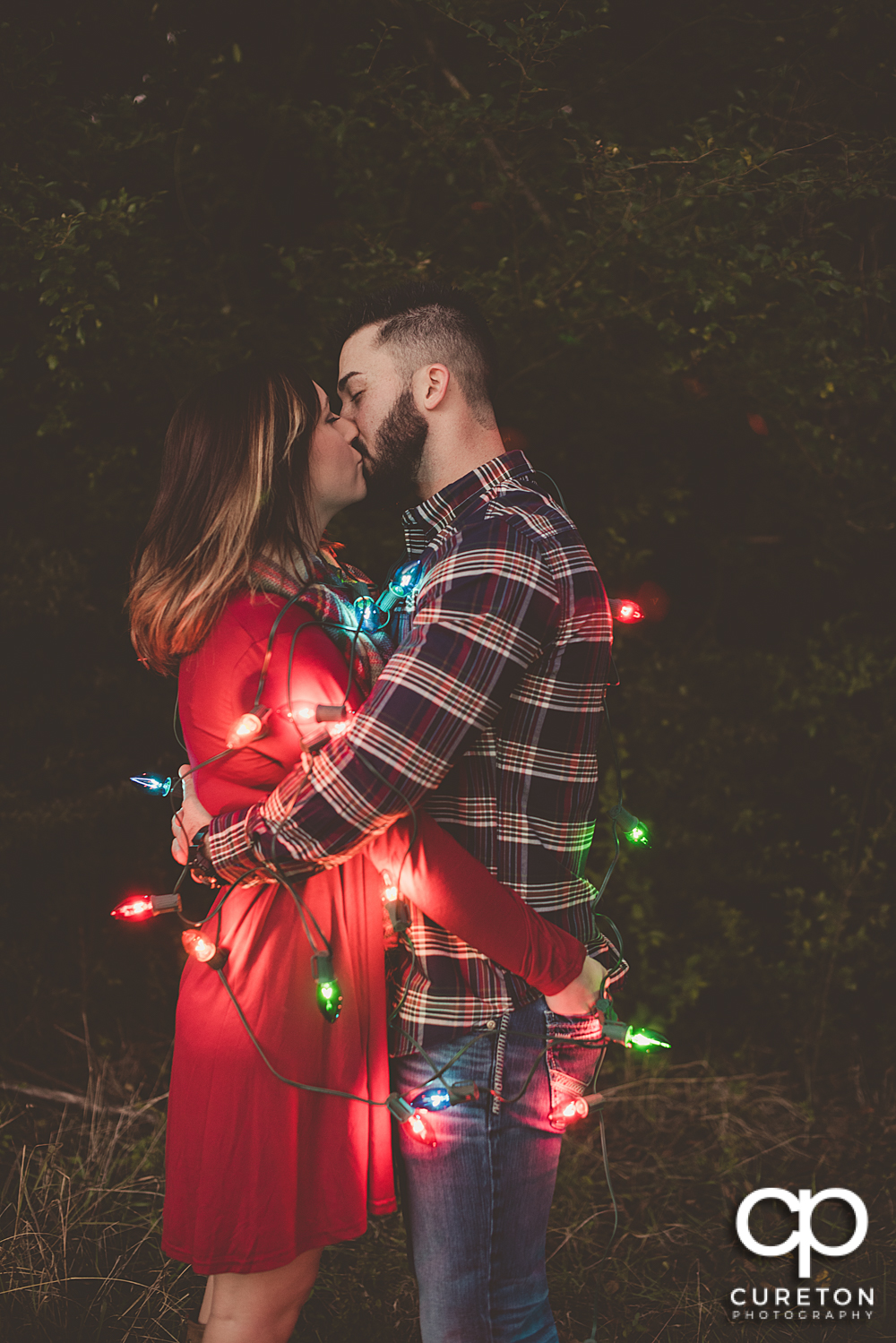 Engaged couple covered in Christmas lights.