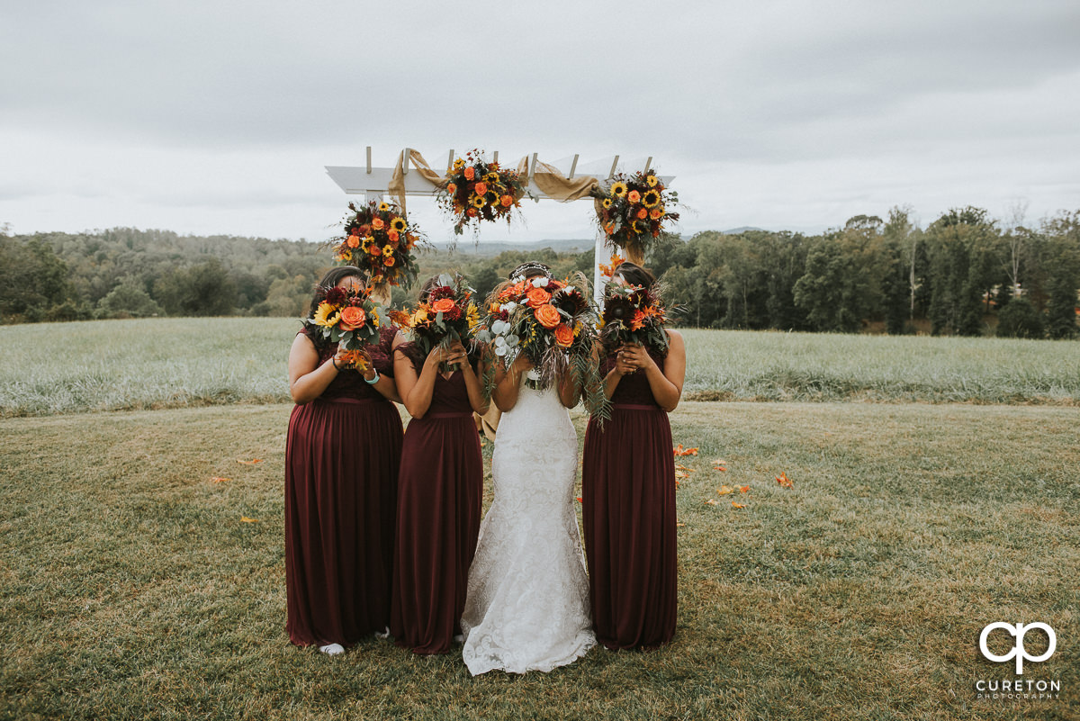 Bridesmaids holding fall bouquets in front of their faces before the wedding.