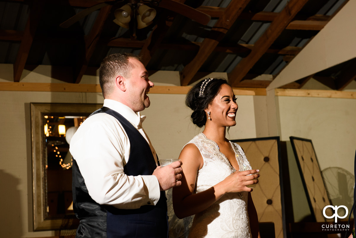 Bride and groom smiling as the maid of honor gives a toast.