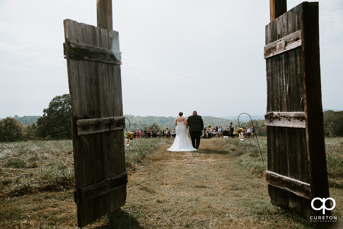 Bride and her father walking out some rustic doors and down the aisle at the wedding at Lindsey Plantation in Taylors,SC.