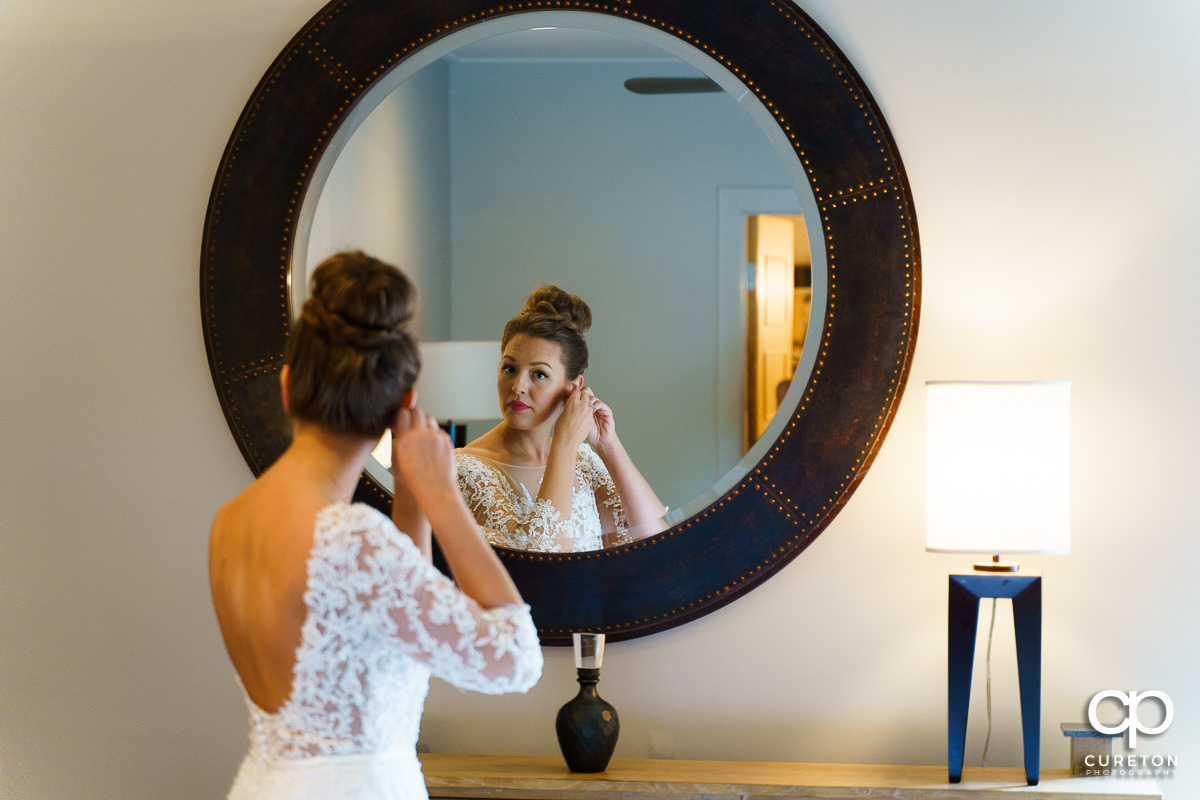 Bride putting her earrings on in the mirror.