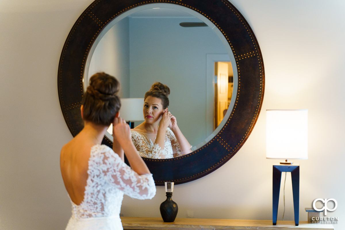 Bride putting her earrings on in the mirror.