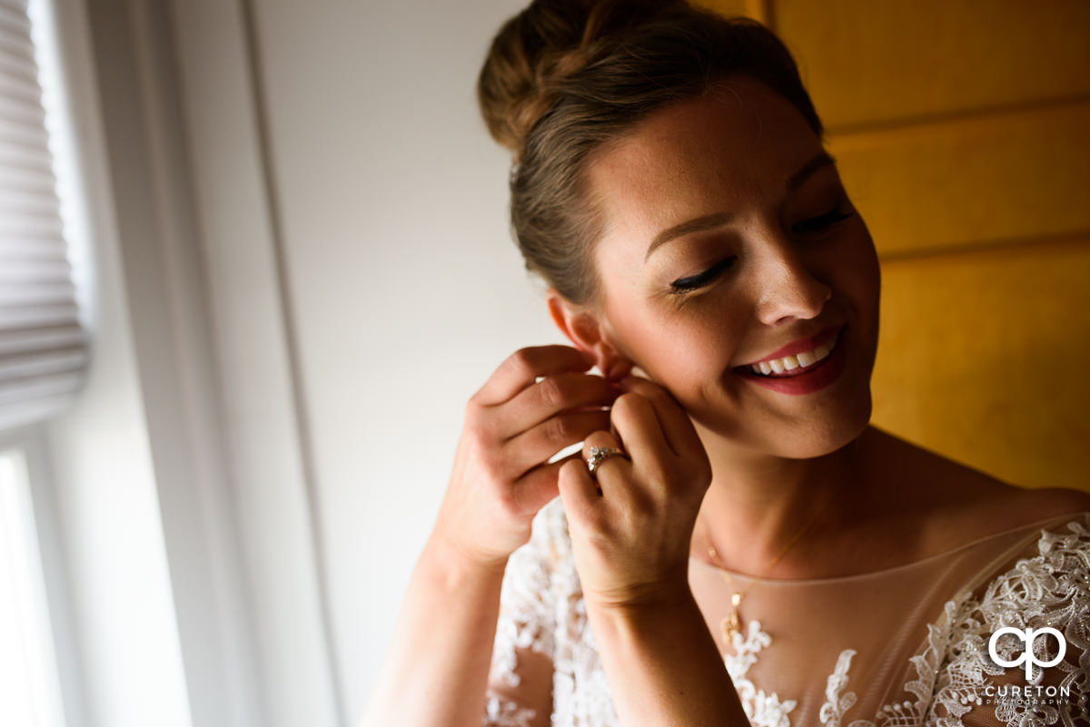 Bride smiling while putting her earrings on.