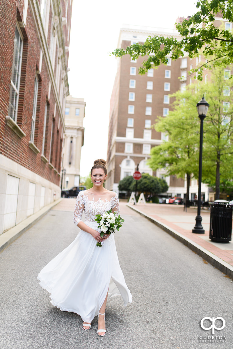 Bride smiling as she walks down the street in downtown Greenville to Soby's Loft for her wedding.