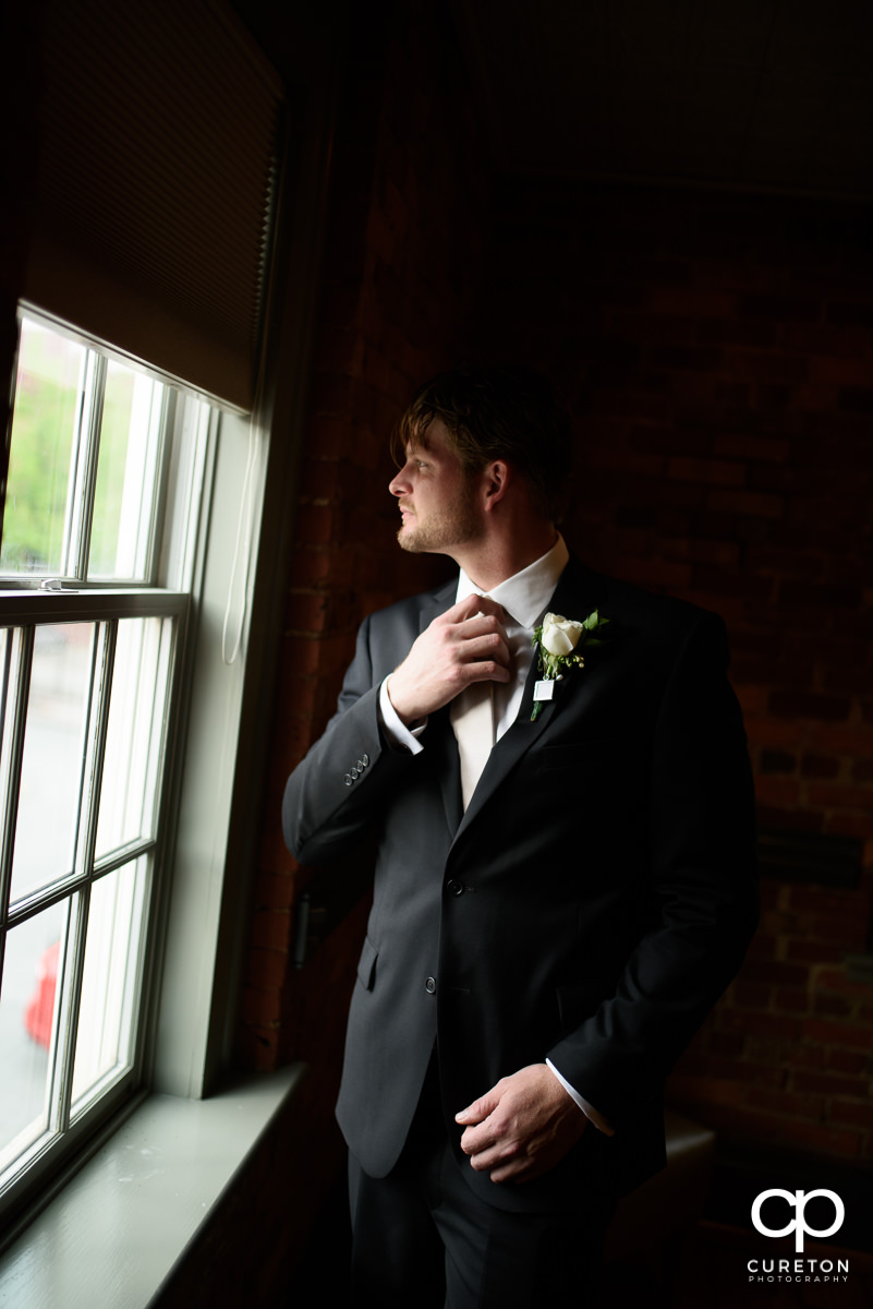 Groom fixing his tie in the window.