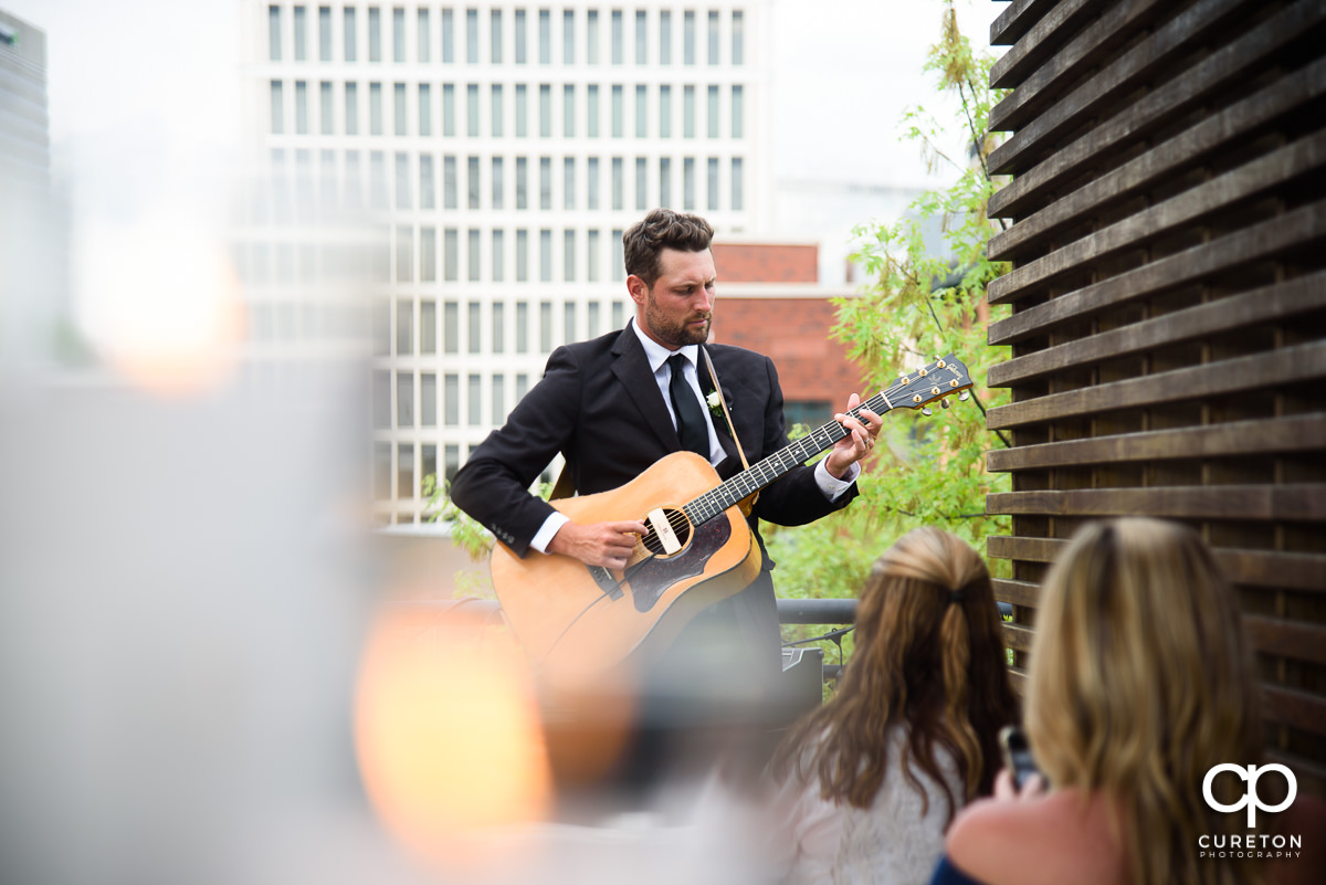 Groomsmen playing guitar at he rooftop ceremony.