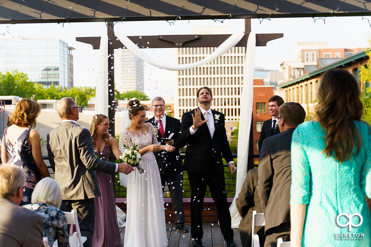 Bride and groom laughing as the guests throw confetti.