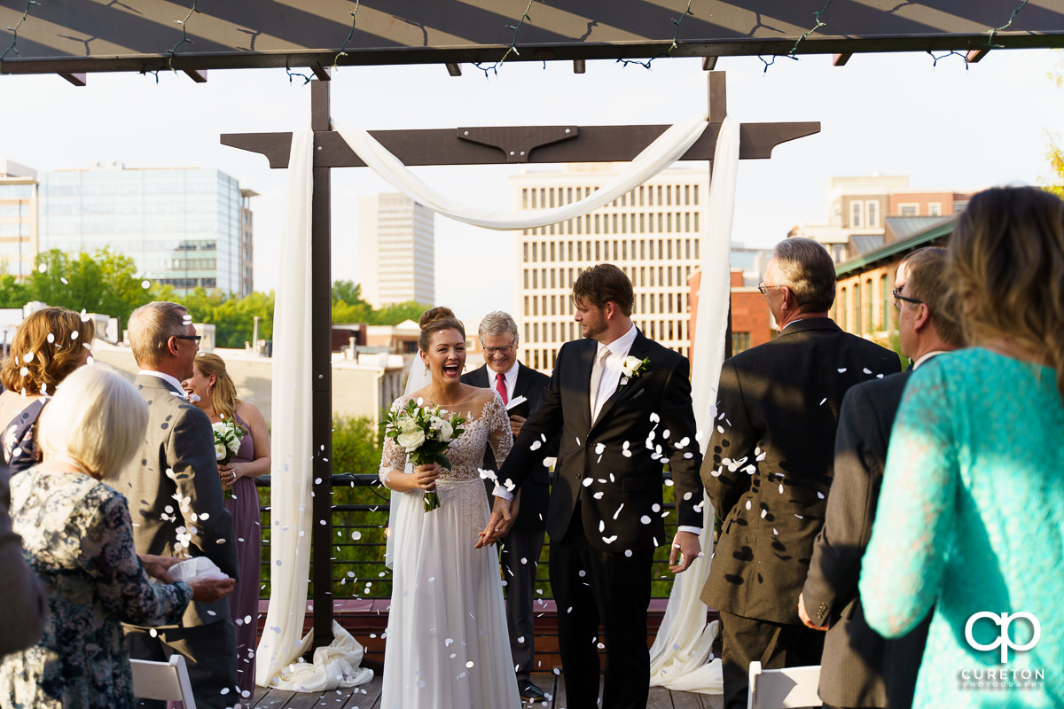 Bride and groom smiling as the wedding guests throw confetti.