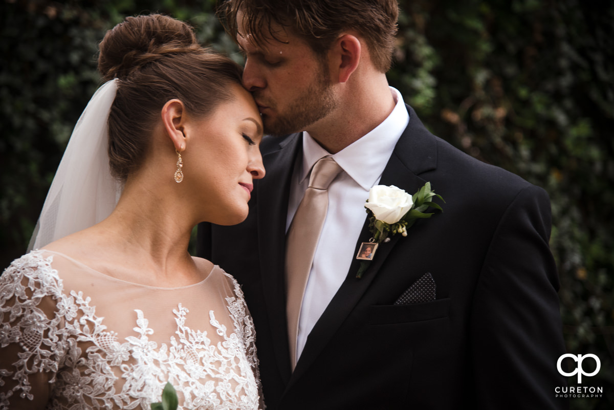 Groom kissing his bride on the forehead in front of a wall of ivy in downtown Greenville,SC.