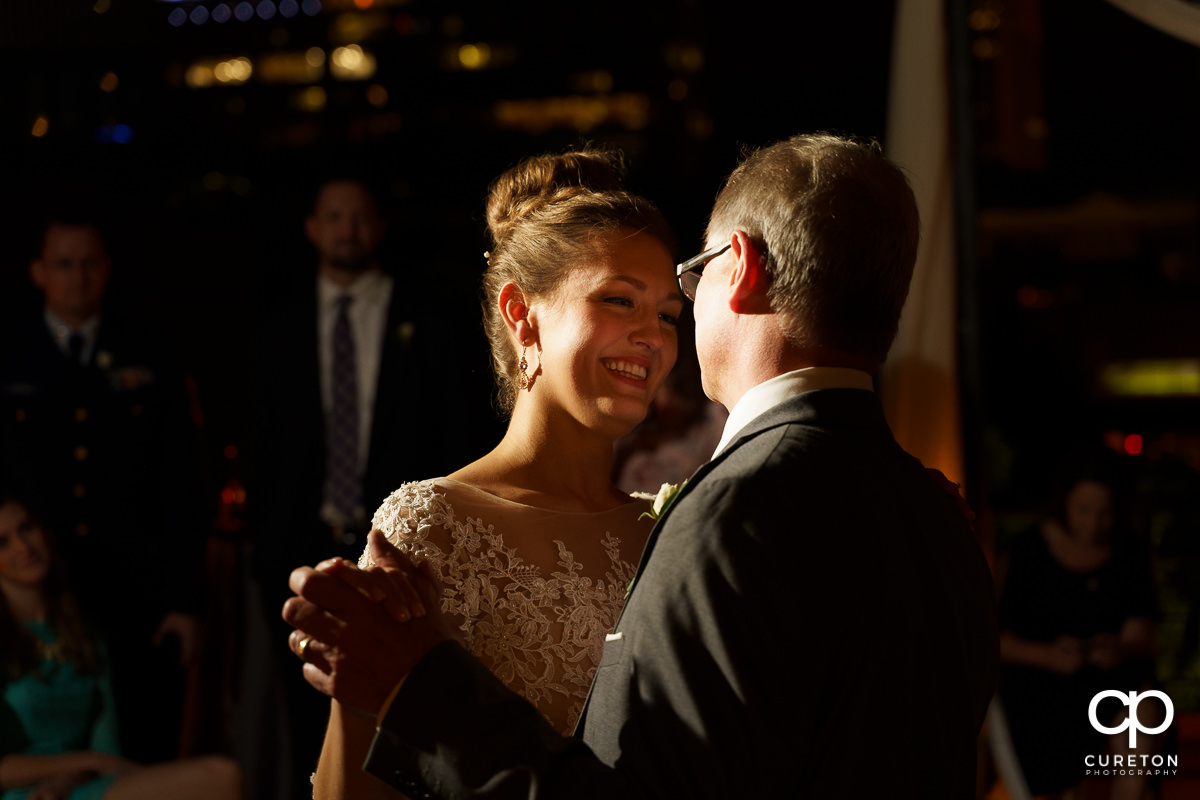 Bride smiling as she shares a dance with her father .