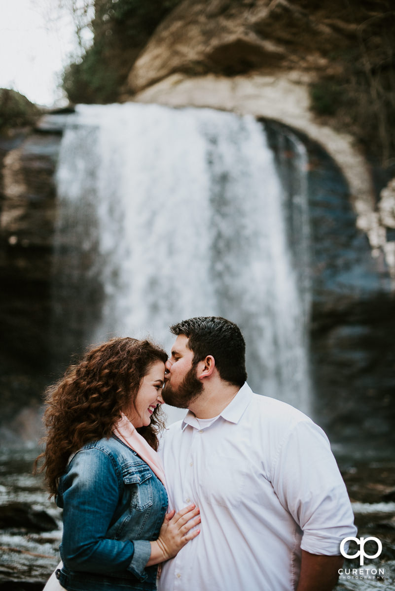 Groom kissing his bride on the forehead in a waterfall.