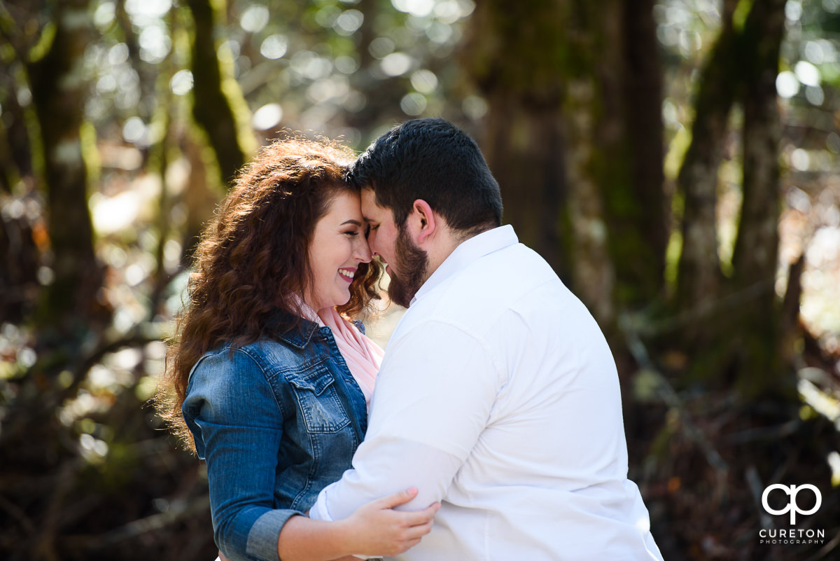 Engaged couple snuggling in the woods.