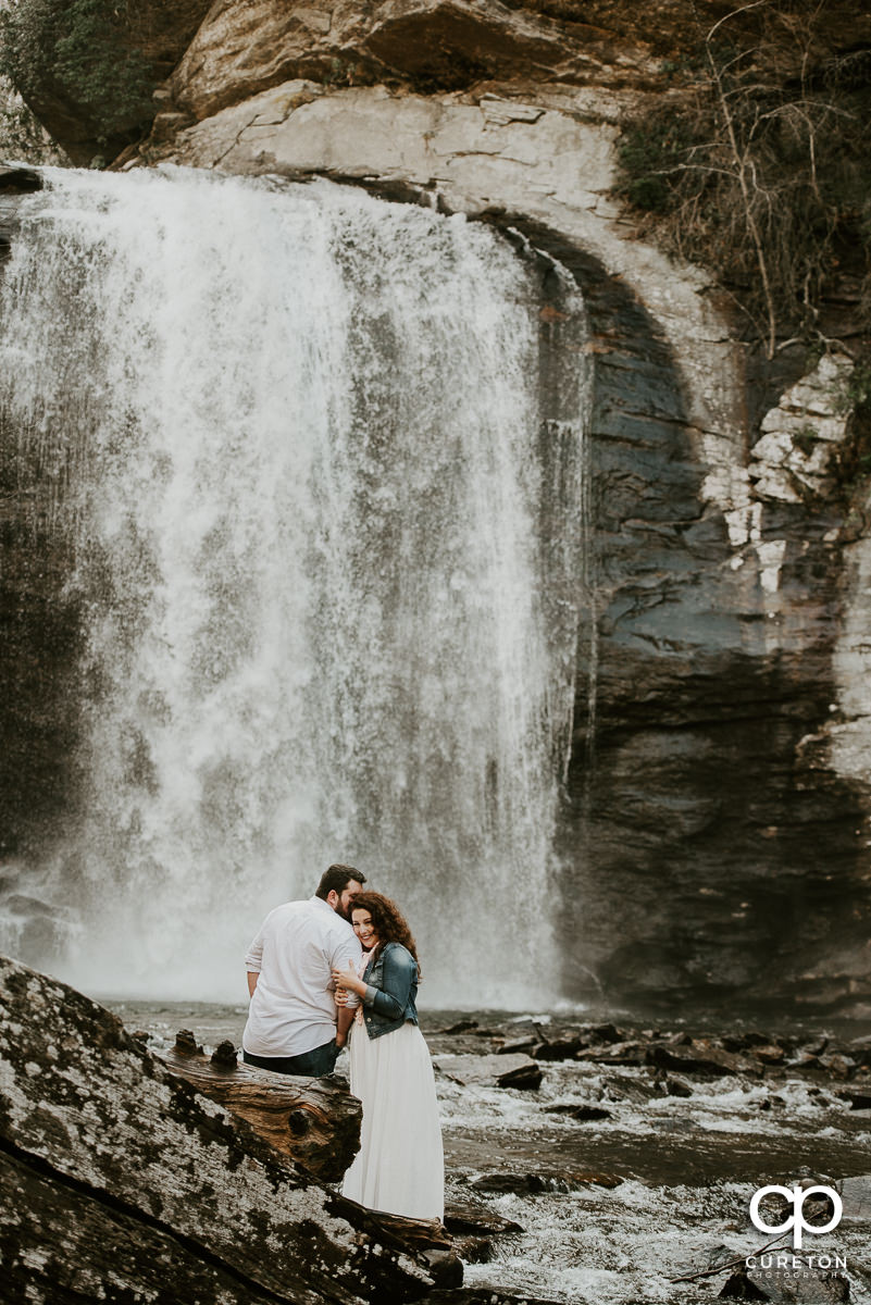 Bride leaning her head on her fiancee's shoulder while standing in the middle of Looking Glass Falls in North Carolina.