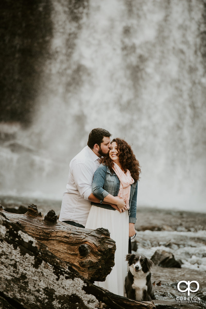Soon to be married couple and their dog in front of Looking Glass Falls during their engagement session at Looking Glass Falls in Pisgah Forest.
