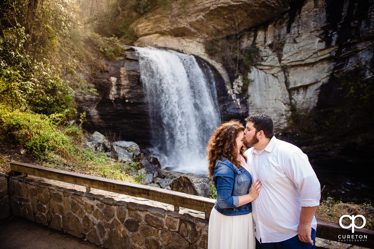 Groom kissing his bride on the forehead at the overlook of the waterfall.