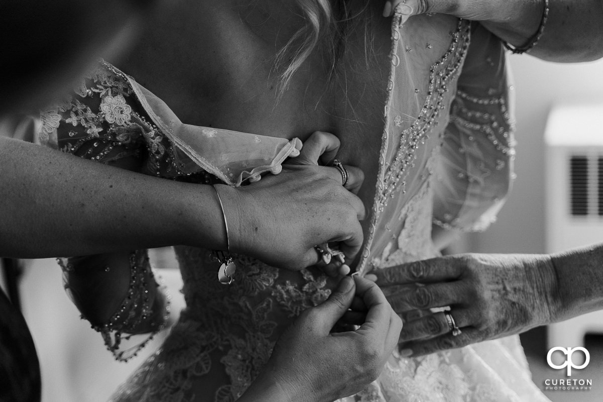 Hands on the back of the bride buttoning her dress.