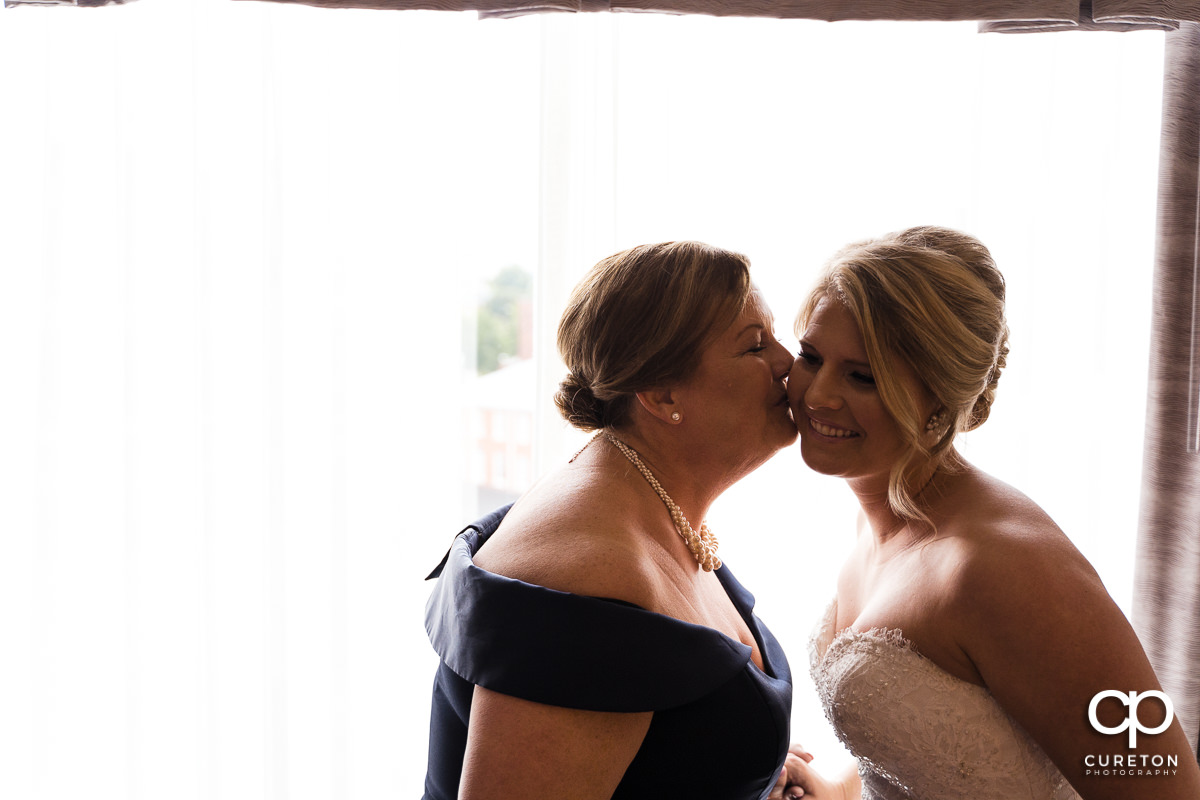 Bride's mom kissing her on the cheek.