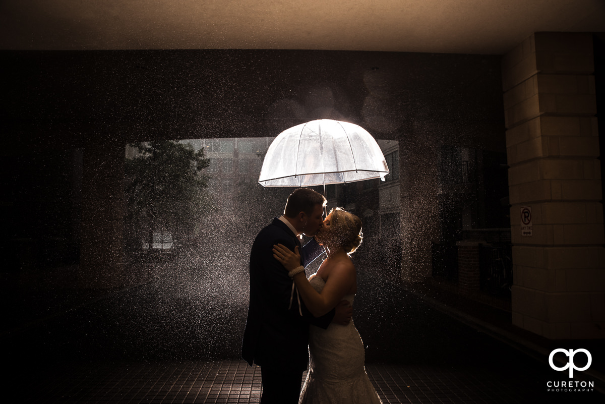 Bride and groom sharing a kiss in the rain before their Mary's at Falls Cottage wedding in downtown Greenville,SC.