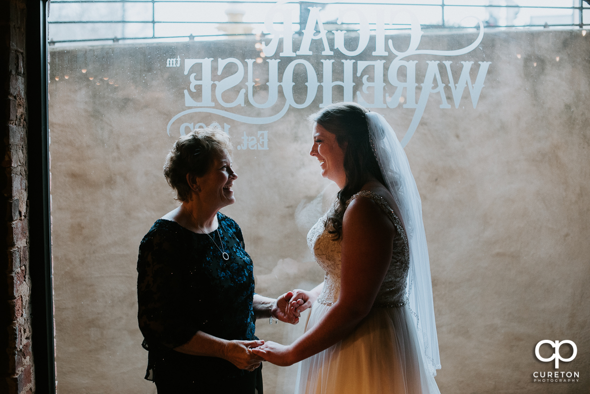 Bride and her mother standing in the window holding hands before the wedding ceremony.