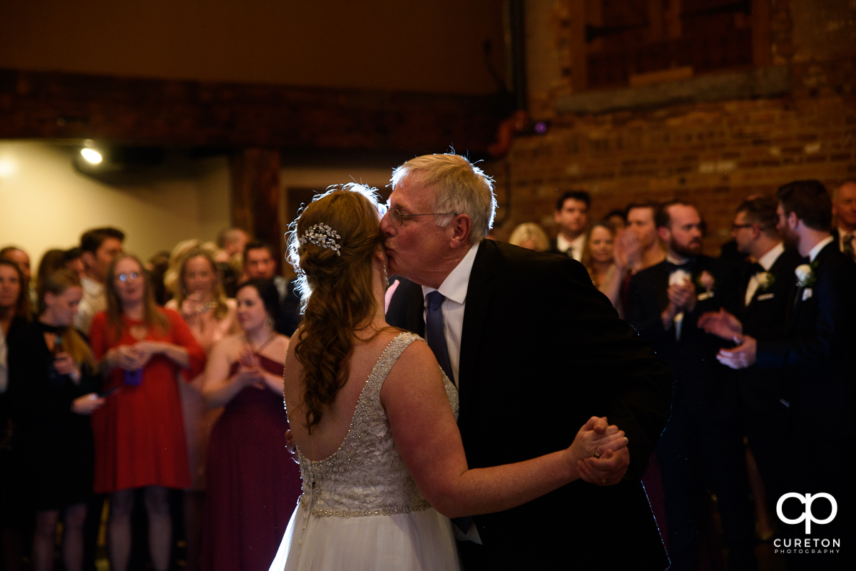 Bride's father kissing his daughter on the cheek.