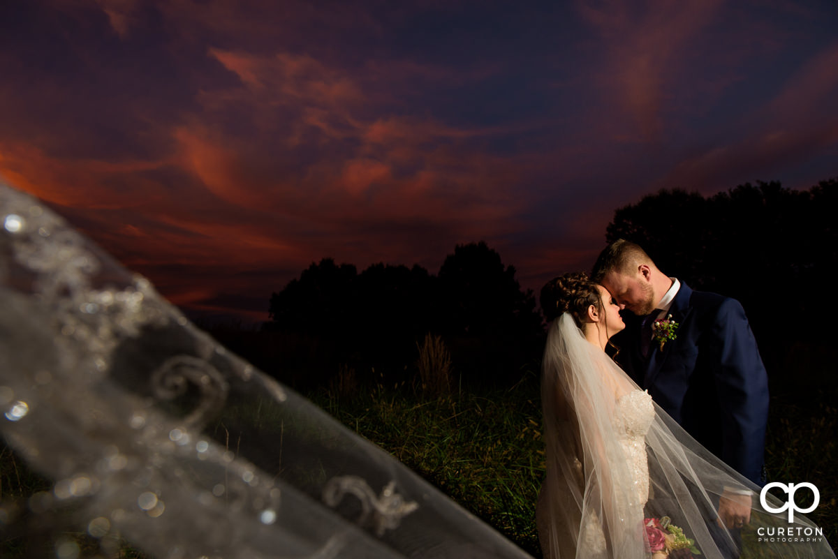 Bride and groom cuddling at sunset while her veil blows in the wind at Noah's Event Venue in Mauldin,SC.