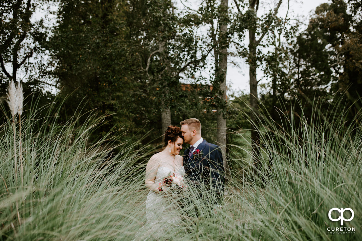Groom and bride standing in some tall grass behind Noah's Event Venue in Mauldin,SC.