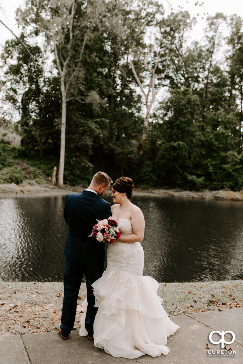 Bride and groom standing by a pond before their wedding ceremony.