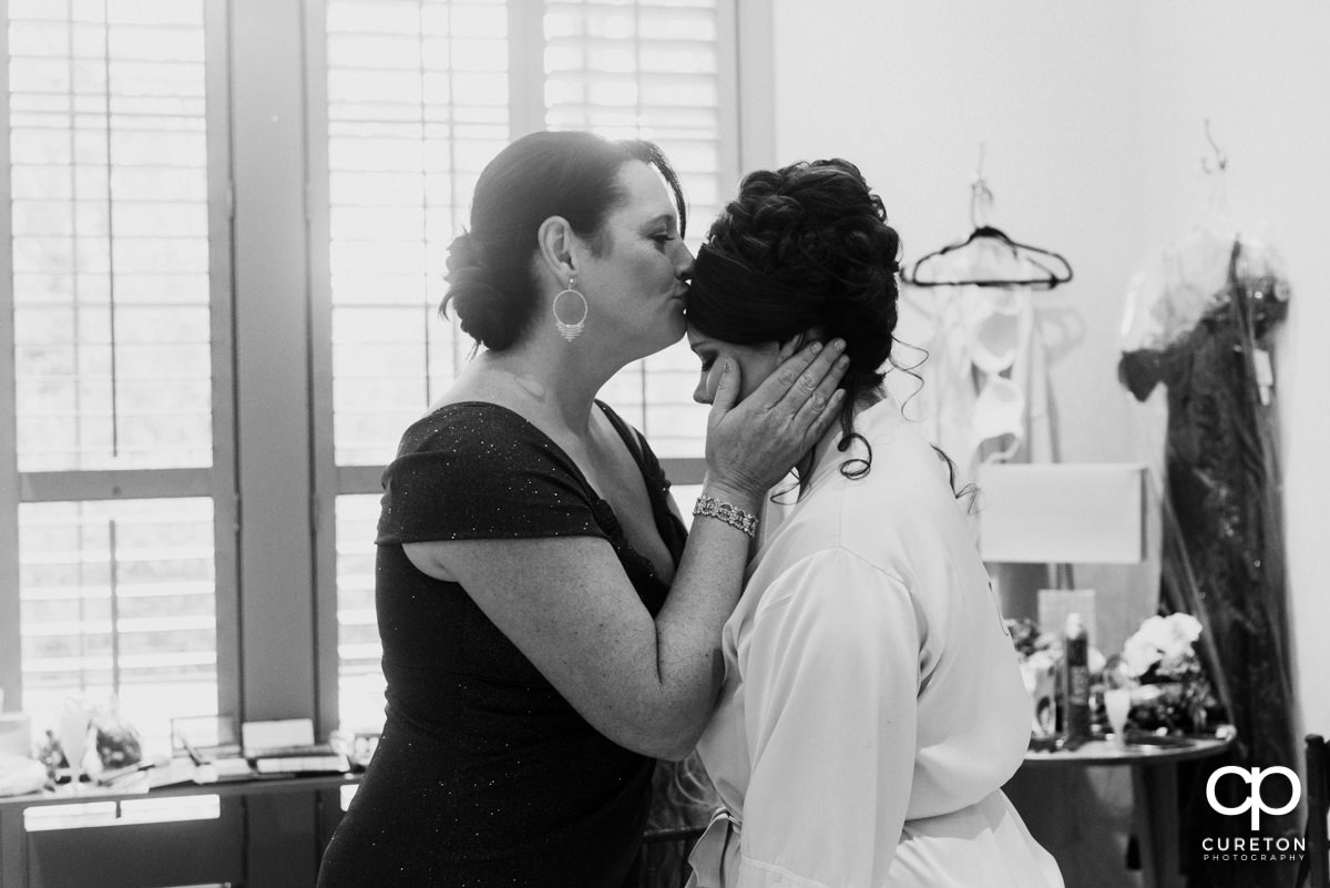 Bride's mother kissing her daughter on the forehead.