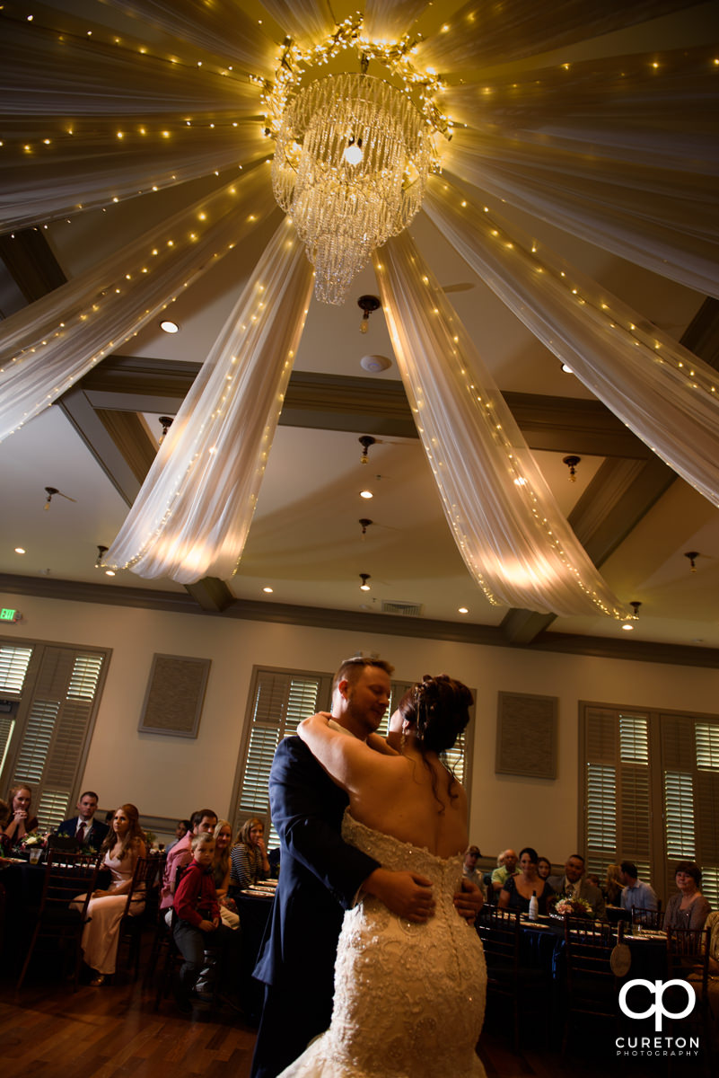 Bride and groom share a first dance underneath a chandelier.