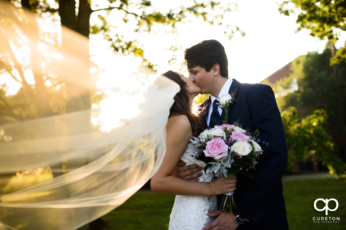 Groom kissing his bride dueing golden hour after their wedding at Noah's Event Venue in Greenville,SC..