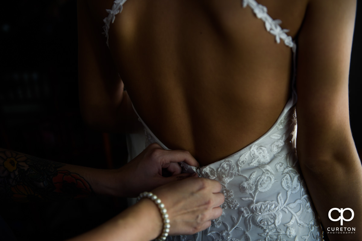 Bride having her dress zipped in the back.