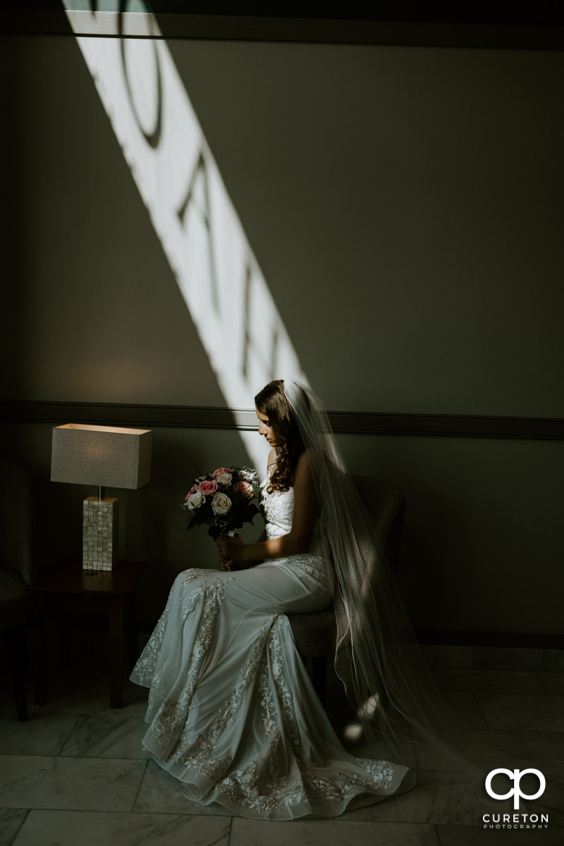 Bride sitting in a patch of light before her wedding.
