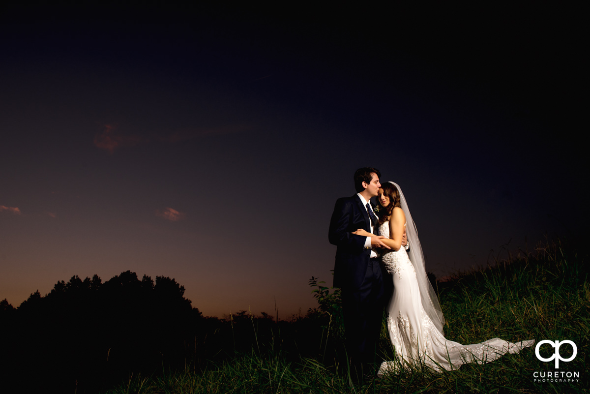 Groom kissing his bride on the forehead at sunset after their wedding at Noah's event venue in Greenville,SC.
