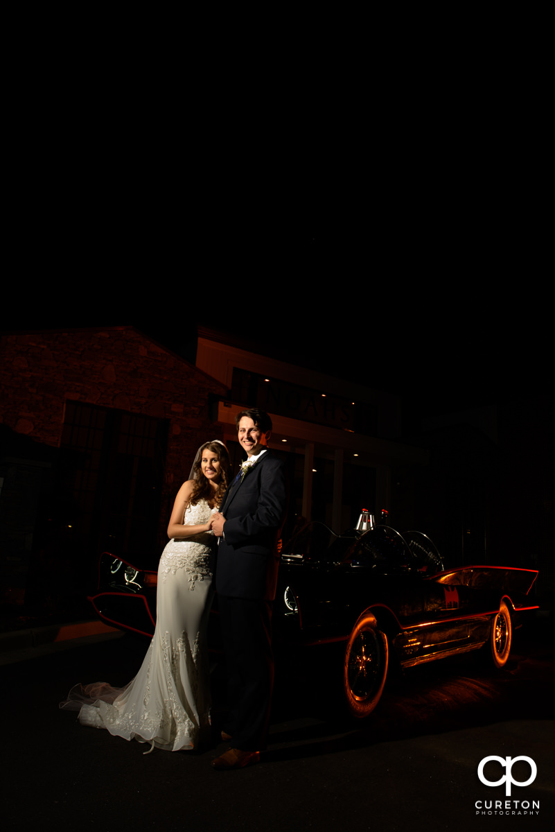 Bride and groom standing beside the batmobile.