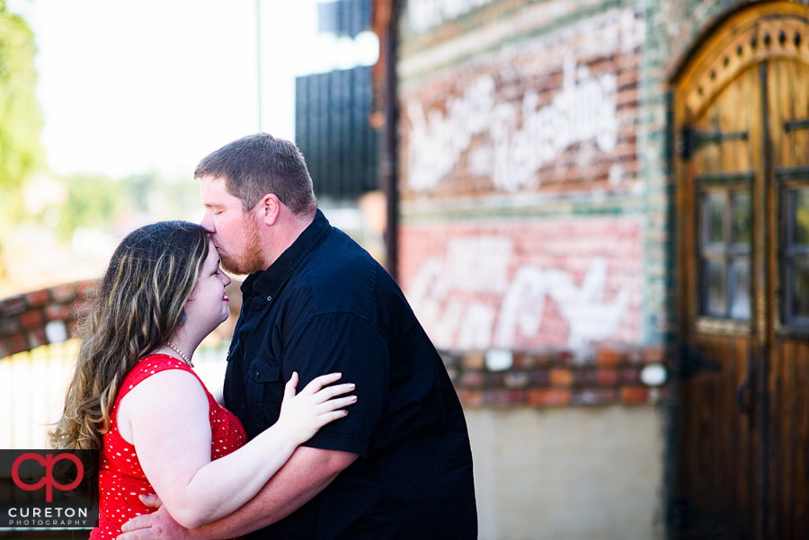 Groom kissing his future bride on the forehead.