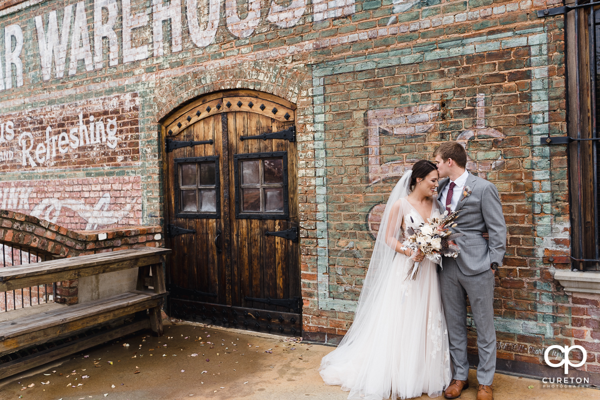 Groom kissing his bride on the forehead before their fall wedding at The Old Cigar Warehouse in Greenville,SC.