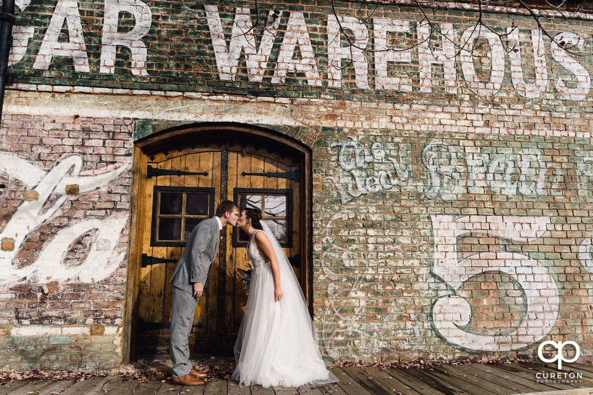 Bride and groom kissing in a doorway on the back deck after their wedding ceremony at The Old Cigar Warehouse in Greenville,SC.