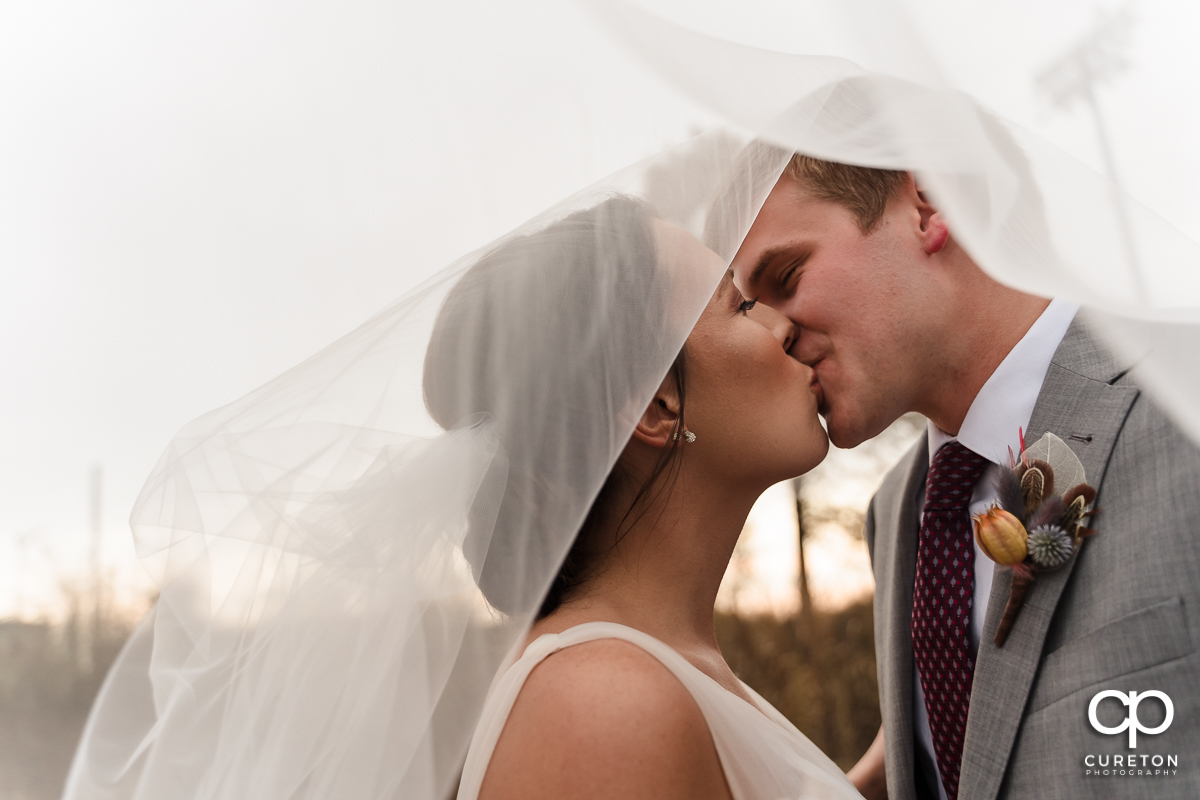 Bride and groom kissing underneath her veil.