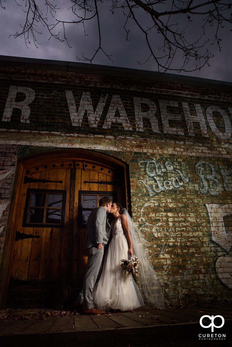 Bride and groom kissing at night on the back deck of The Old Cigar Warehouse.