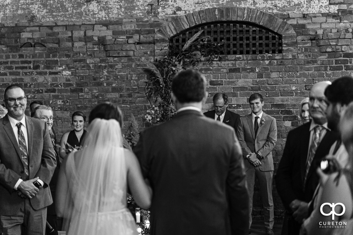 Groom smiling as he sees his bride walking down the aisle on their wedding day.