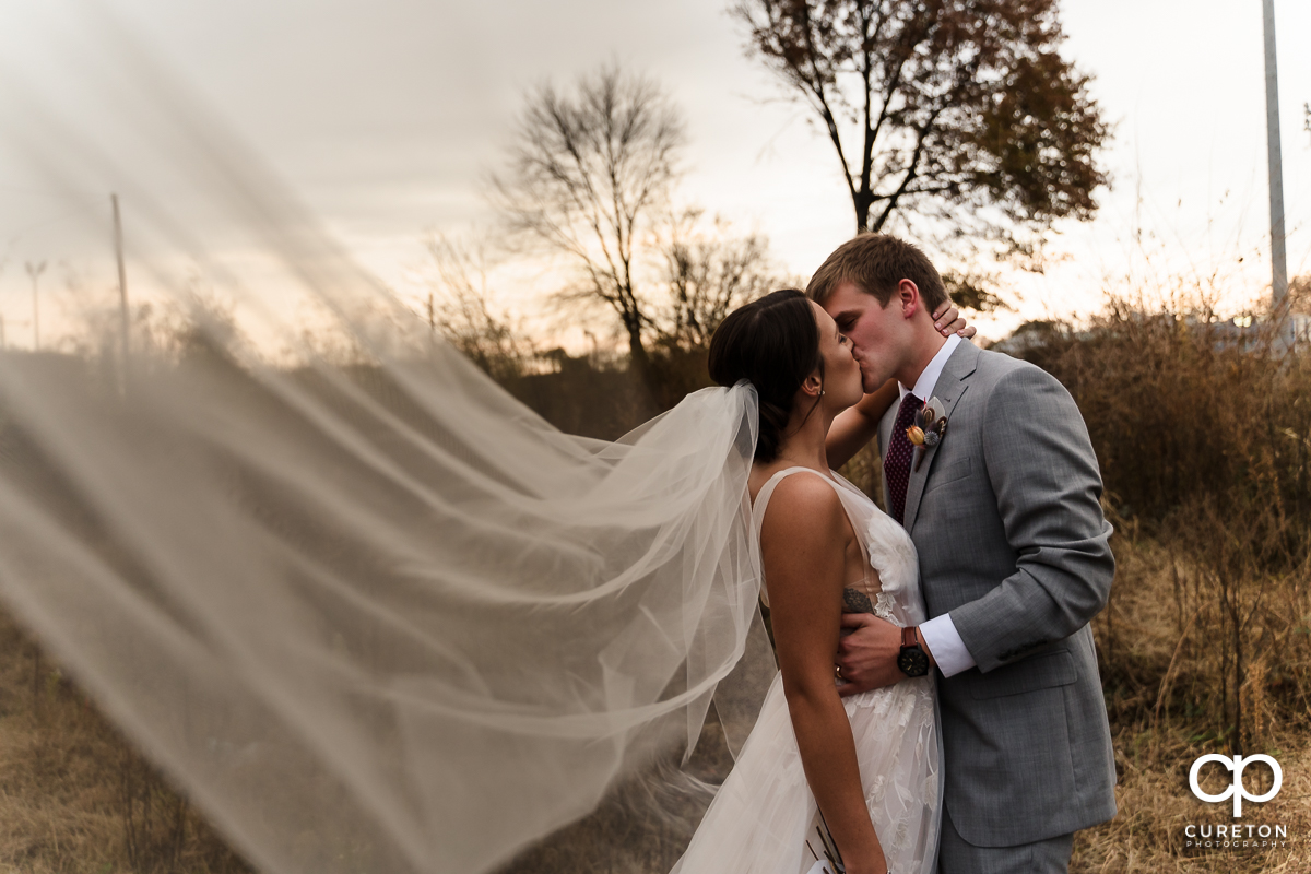 Bride and groom kissing as her veil blows into the breeze.