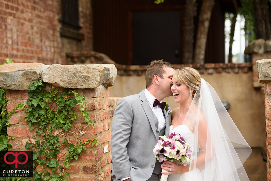 Bride laughing while groom whispers in her ear.