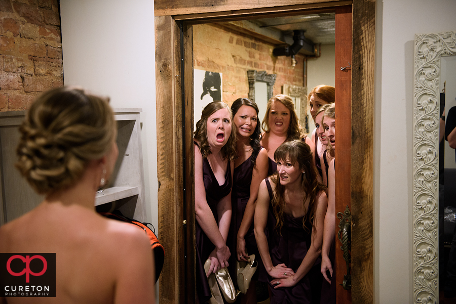 The bridesmaids looking at the bride for the first time faking bad faces.