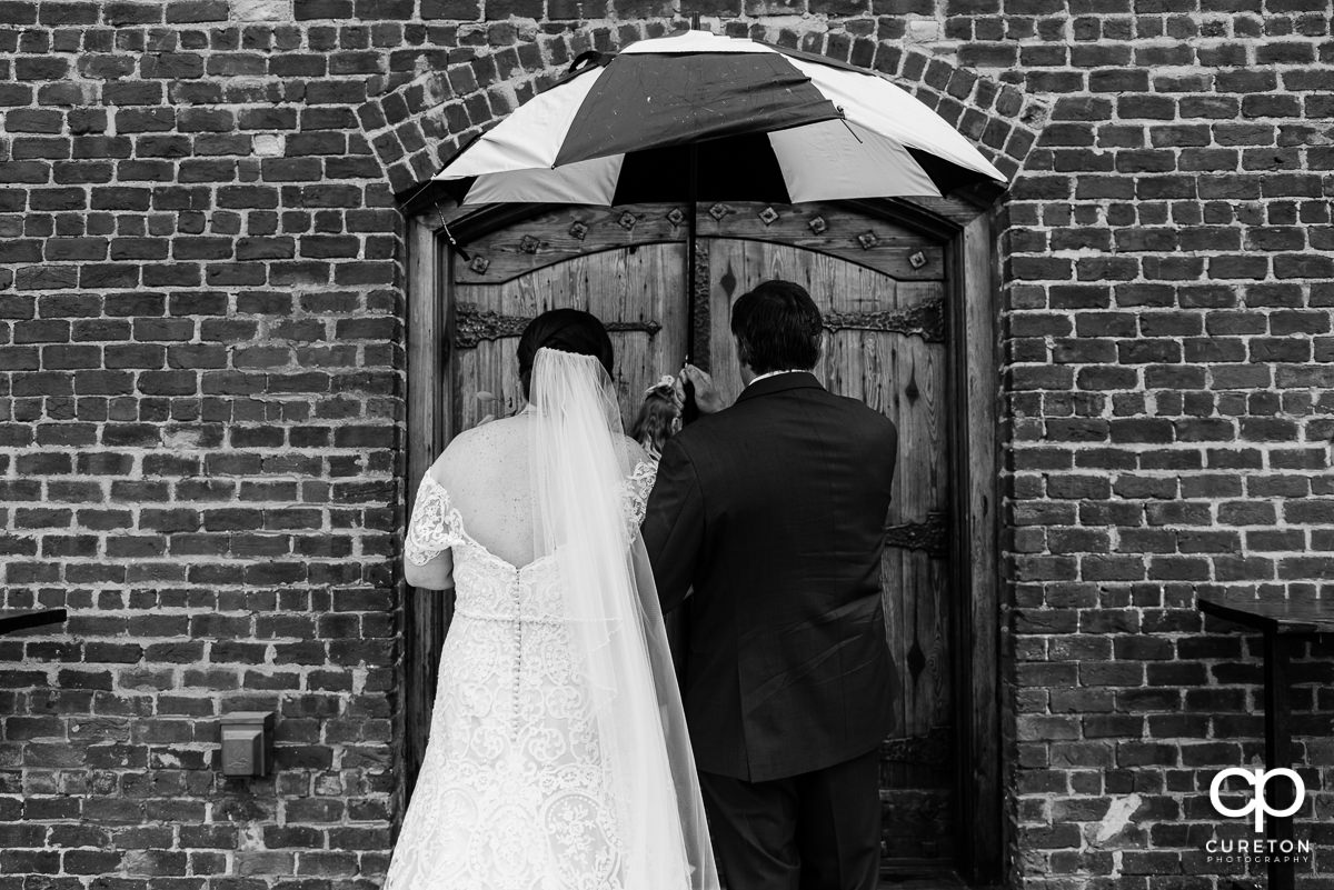 Bride and her father holding an umbrella in the rain preparing to walk down the aisle at her wedding.