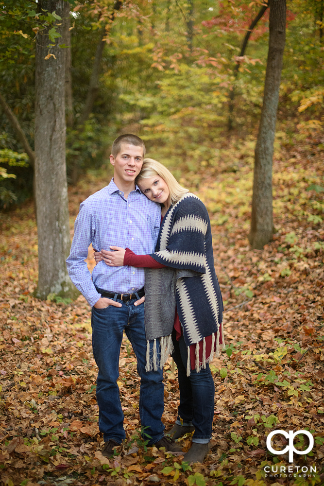 Future bride and groom standing in the fall leaves in the park.